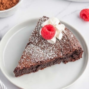 A slice of chocolate cake without flour on a plate and garnished with raspberries.