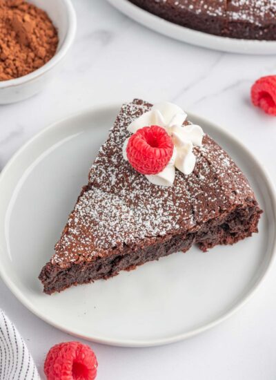 A slice of chocolate cake without flour on a plate and garnished with raspberries.