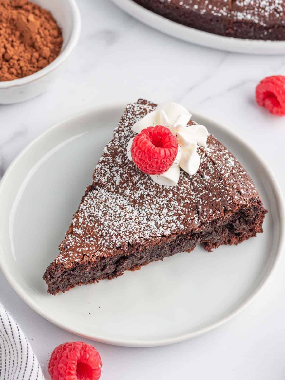 A slice of chocolate cake without flour on a plate and garnished with raspberries.