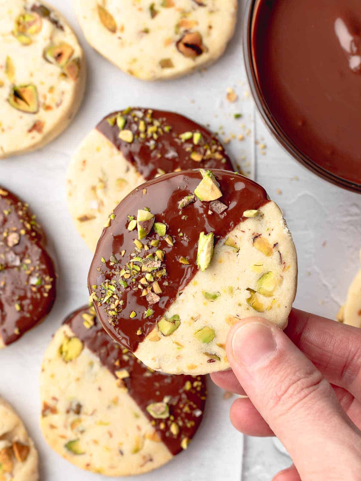 Pistachio cookie dipped halfway in melted dark chocolate with chopped pistachios.