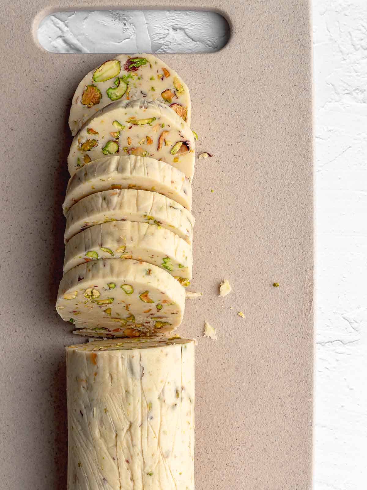 Chilled pistachio cookie dough log cut into thick rounds on a cutting board.