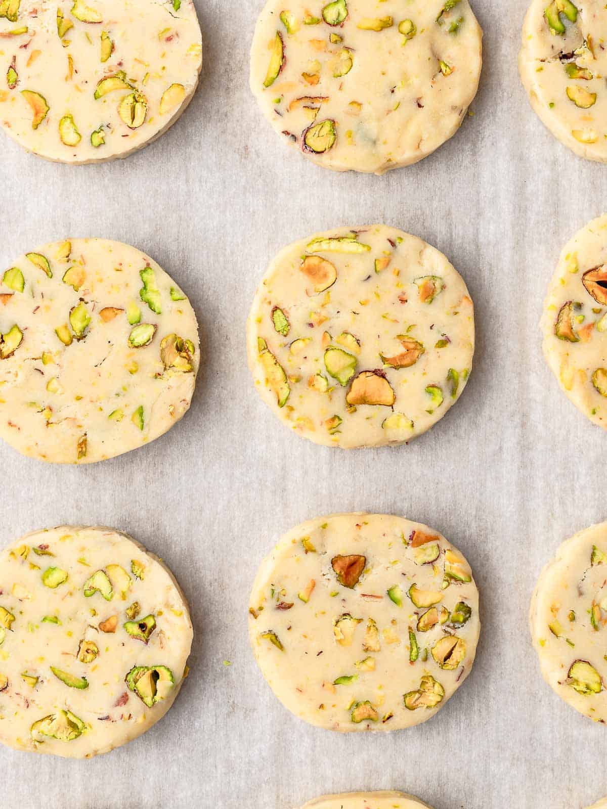 Sliced pistachio cookies arranged on a parchment-lined baking sheet.