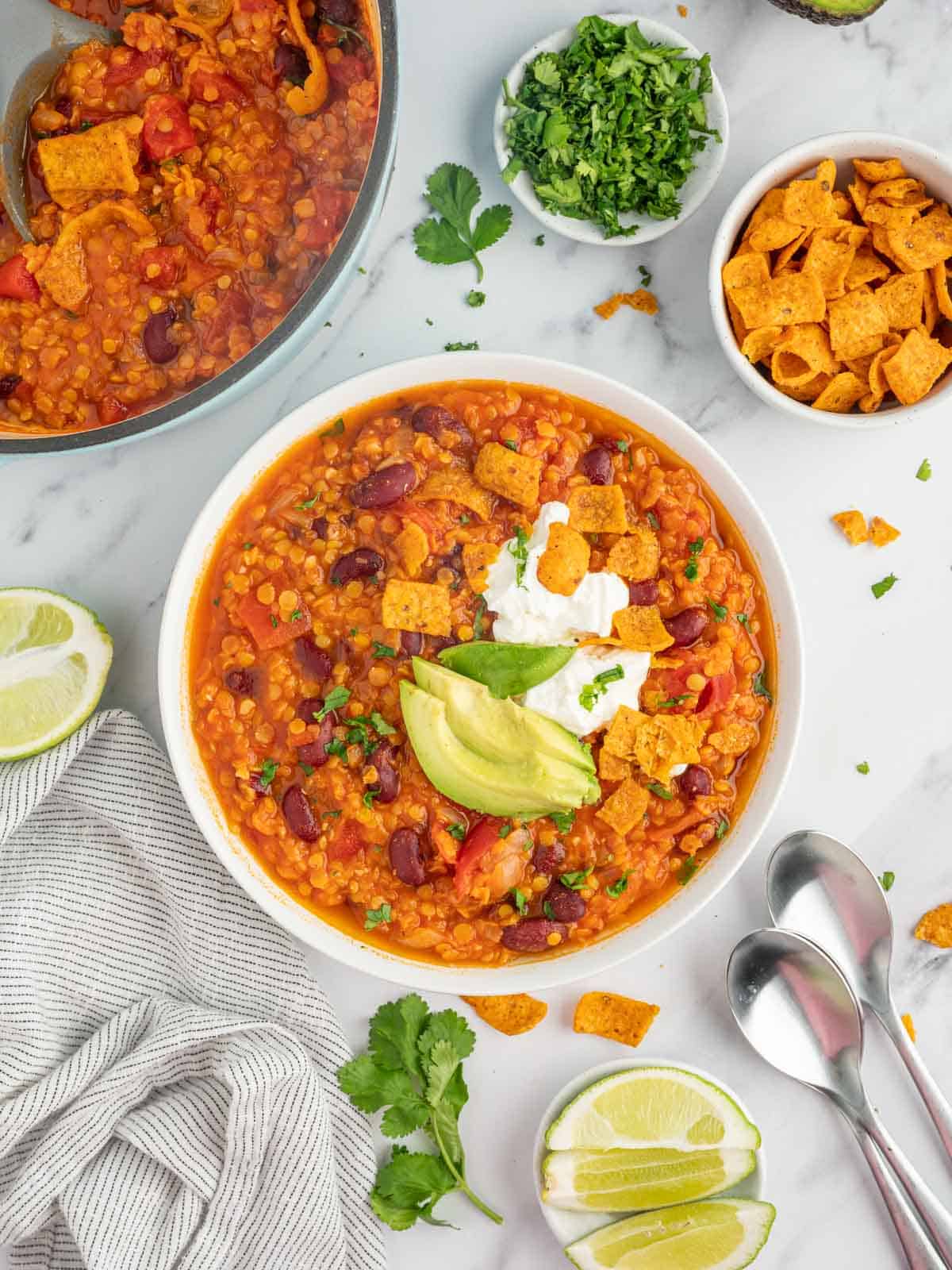 A bowl of meatless chili with spoons and toppings.