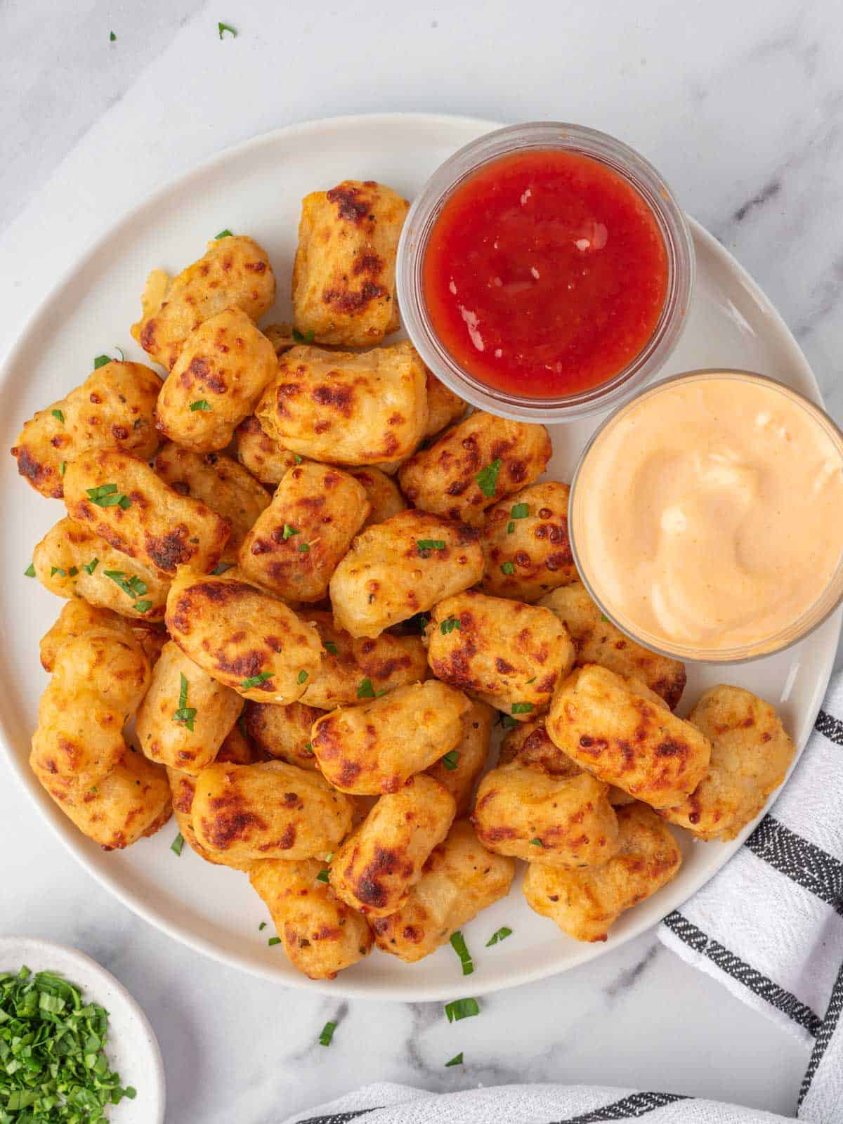 A plate of golden tater tots with dipping sauce.