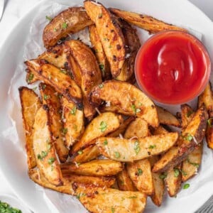 A plate of potato wedges air fryer with ketchup for dipping.