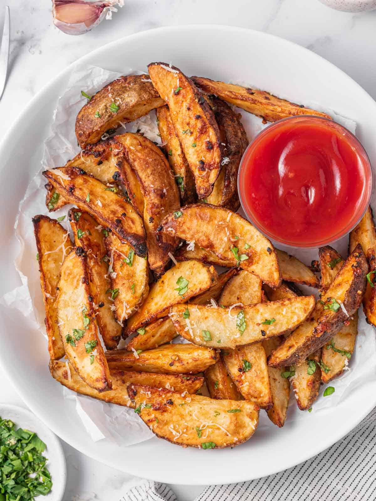 A plate of potato wedges air fryer with ketchup for dipping.