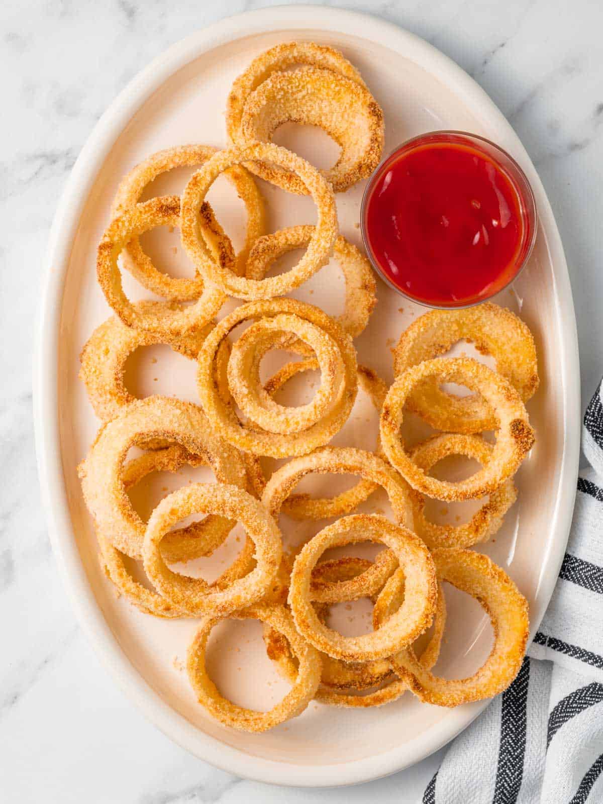 A pile of homemade onion rings oven on a plate with ketchup.