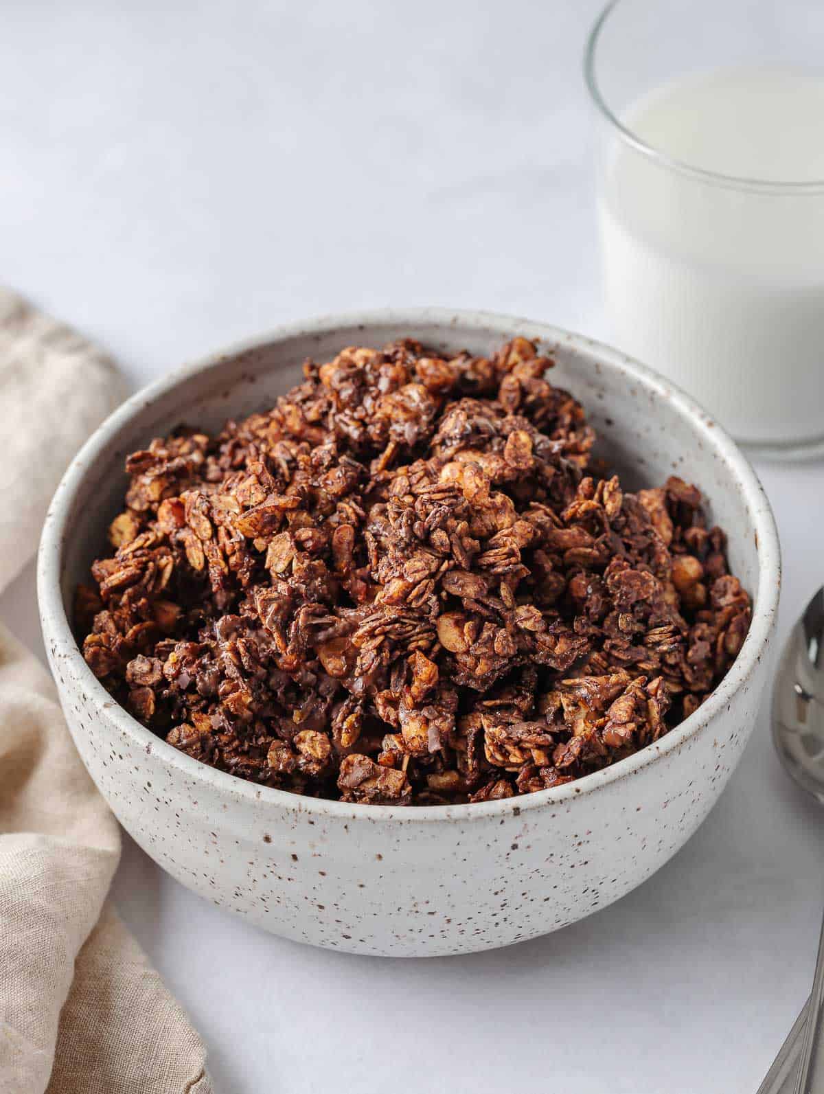 A bowl of chocolate granola with milk in a cup.