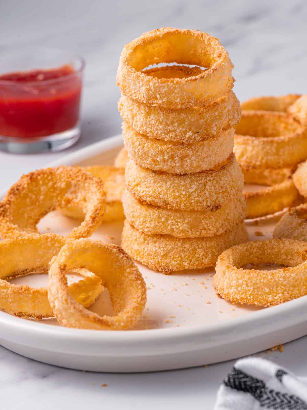 A stack of crispy baked onion rings with ketchup in the background.
