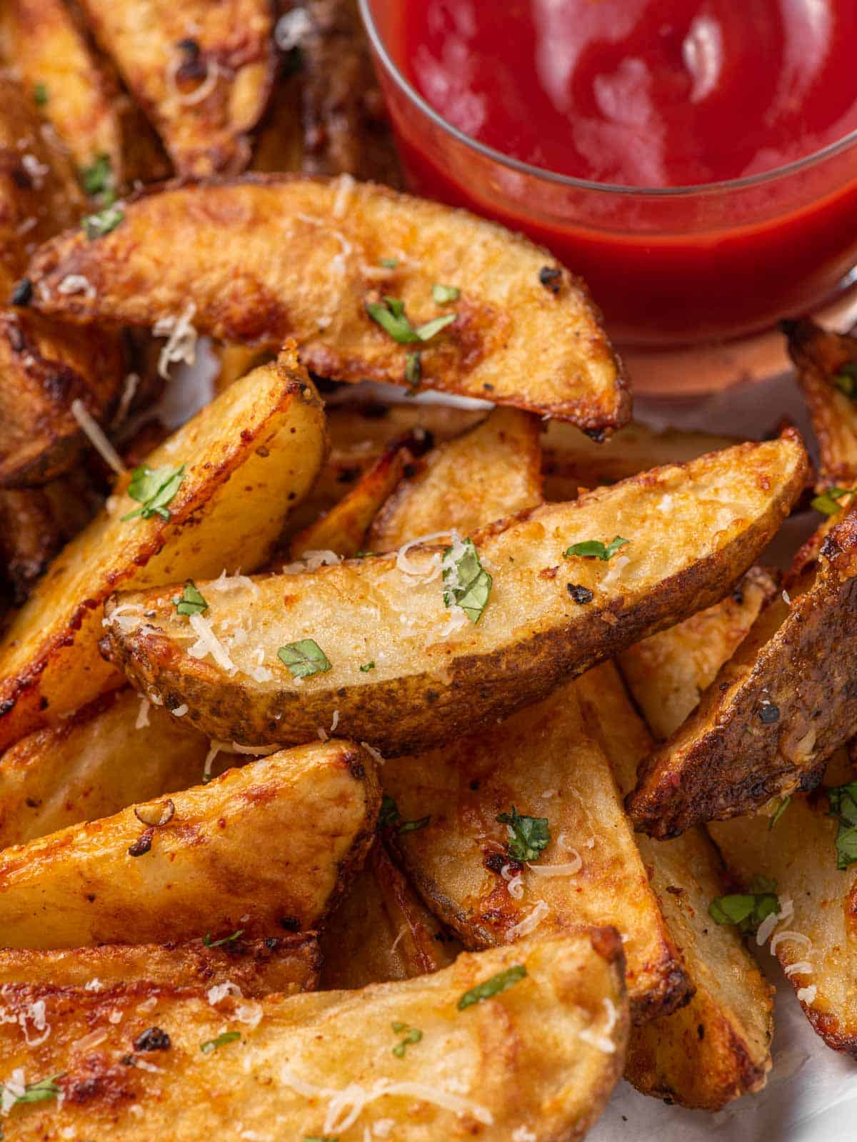 A close up of crispy parmesan potato wedges with ketchup.