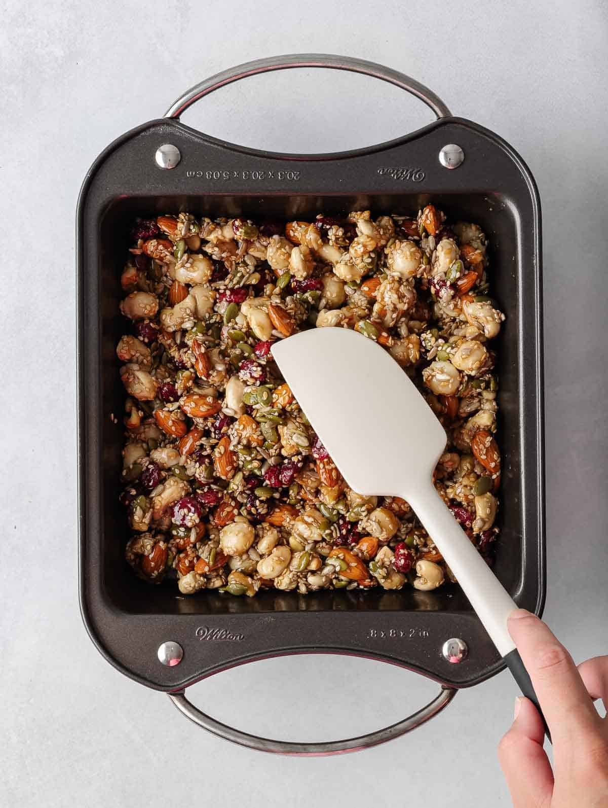 A spatula presses the healthy nut bar recipe into a pan.