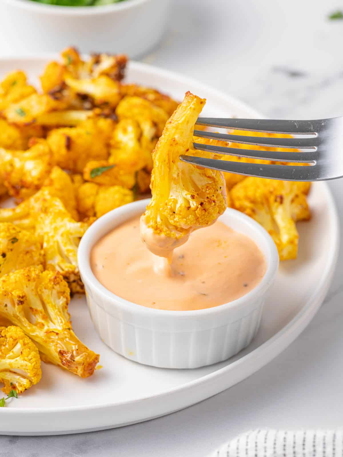 A fork dips a cauliflower bite into sauce.