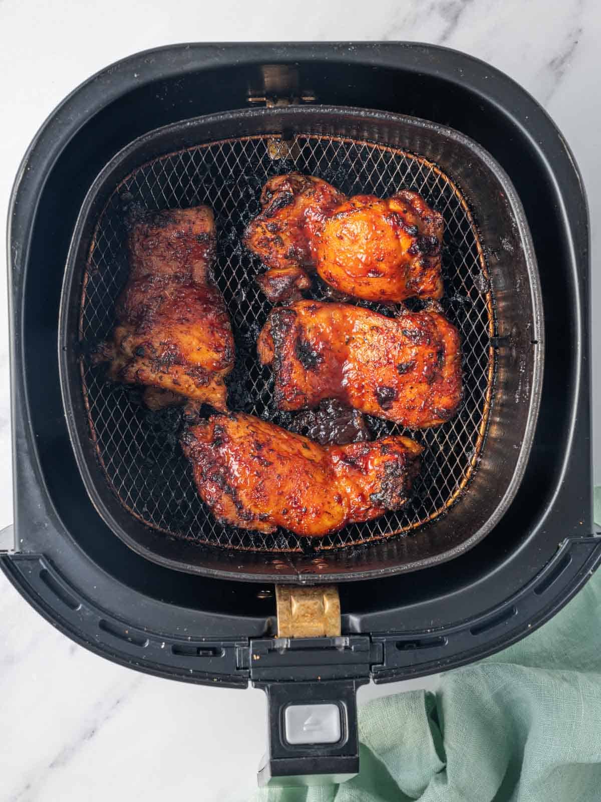 Finished bbq chicken thighs resting in an air fryer basket.