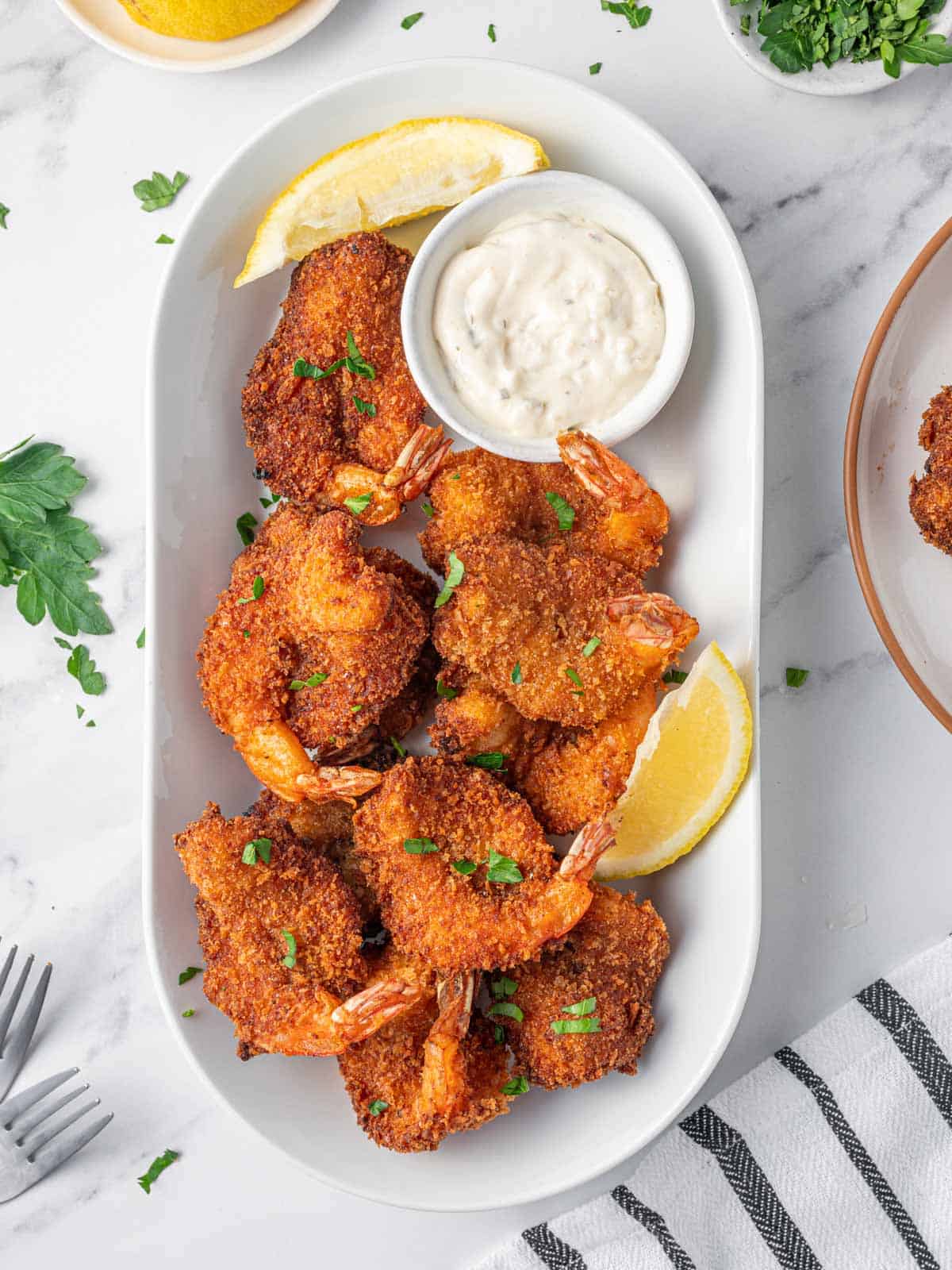 Fried butterfly shrimp on a platter with lemon wedges and tarter sauce.