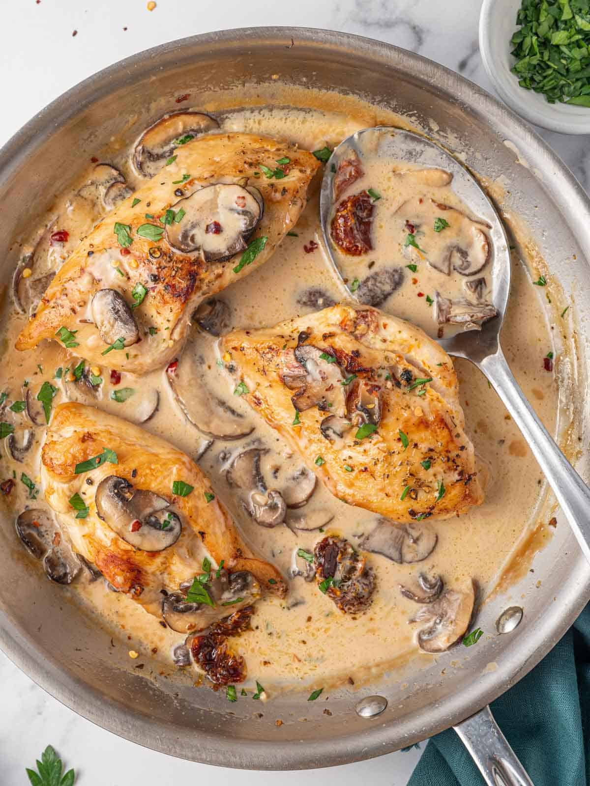 A spoon ladles marsala cream sauce over stuffed chicken breast.