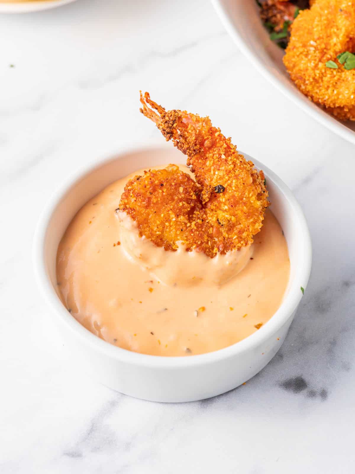 A bowl of dip with a keto breaded shrimp.