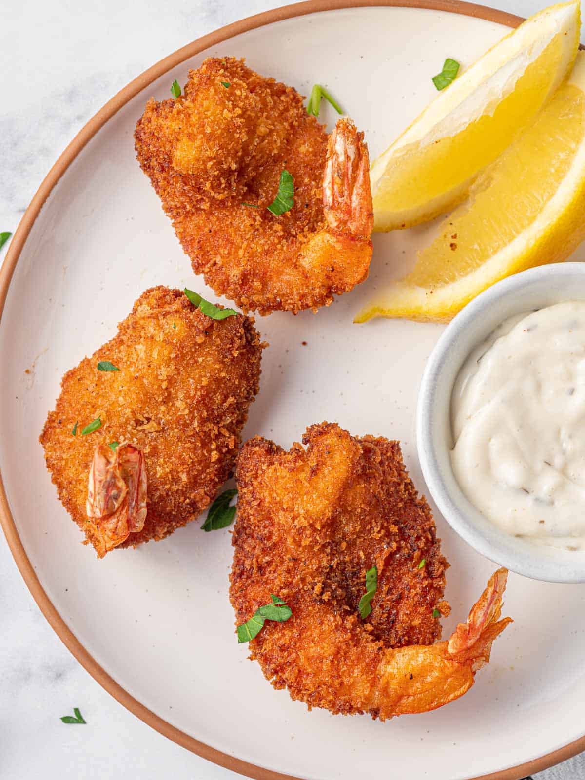 Three pan fried butterfly shrimp on a plate with tarter sauce.