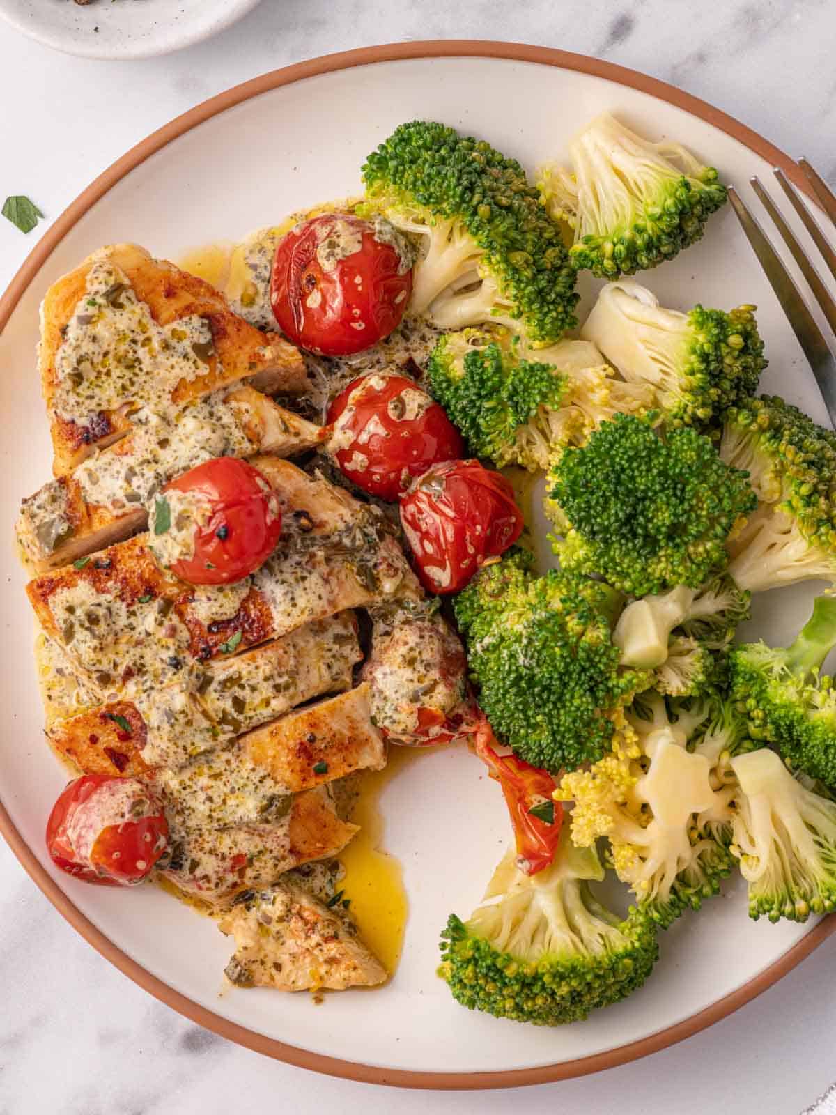 A plate with sliced pesto cream chicken and broccoli.
