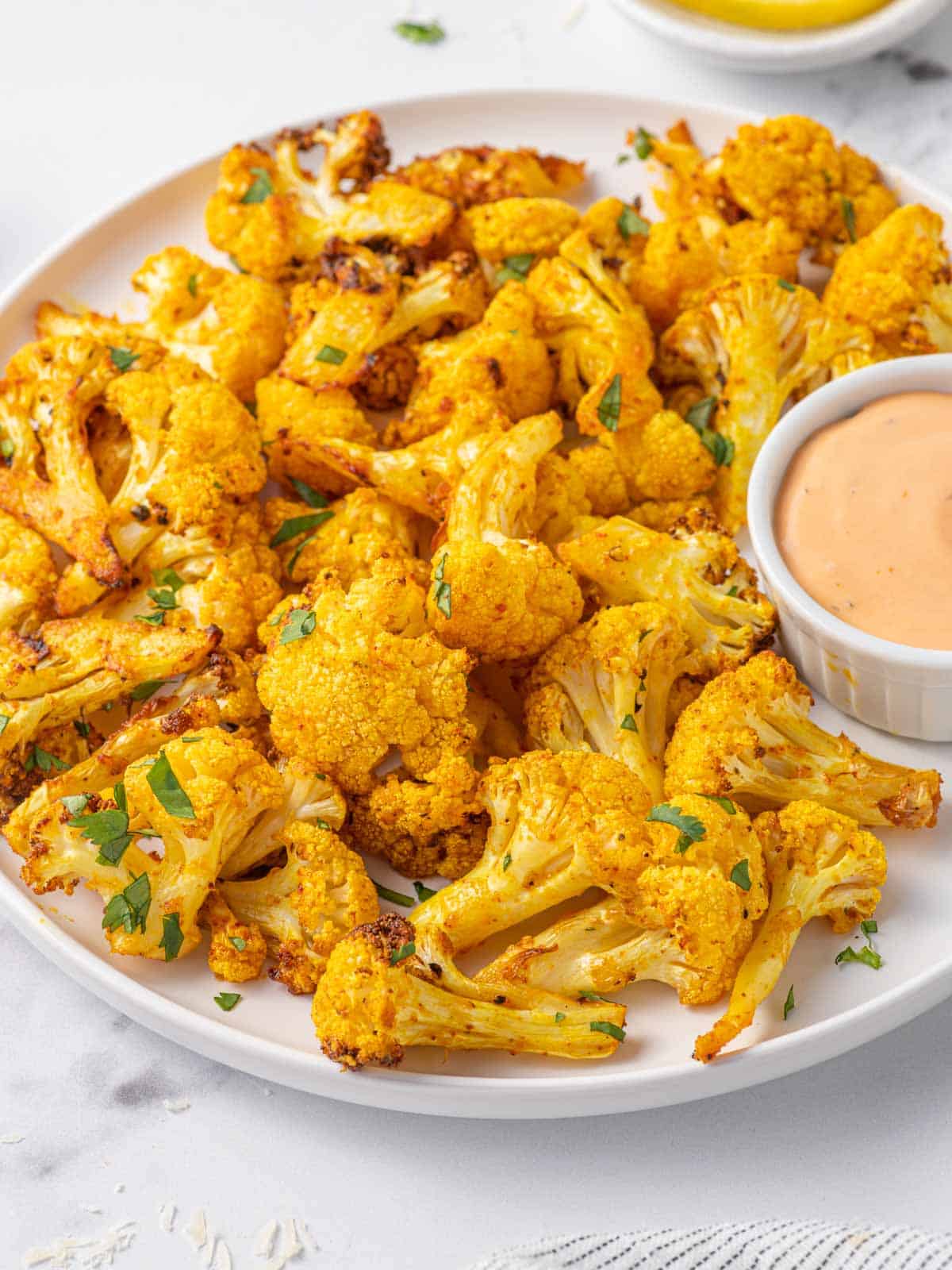 A plate of roasted cauliflower bites with dipping sauce.