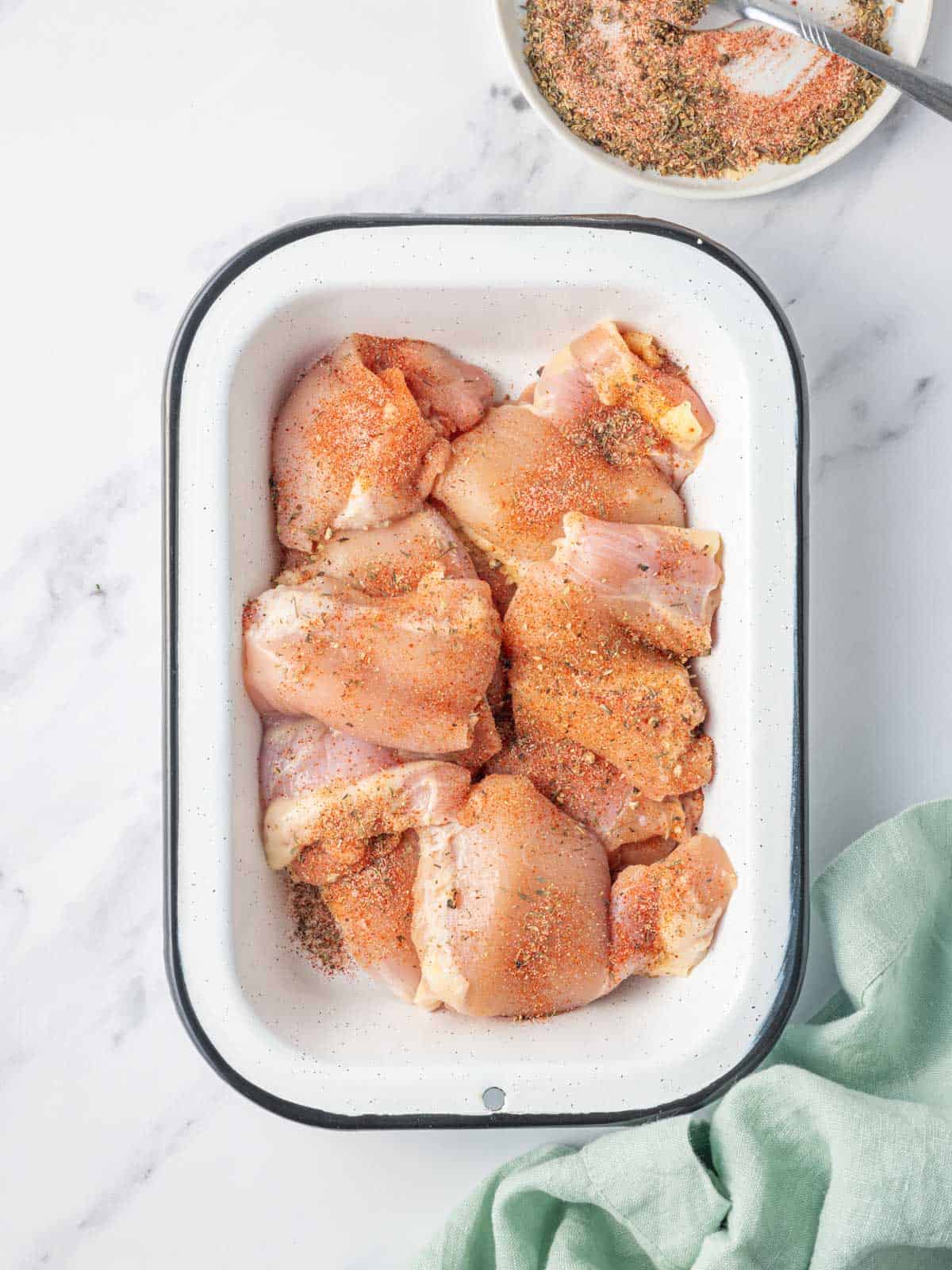 Seasoning raw chicken thighs in a dish.