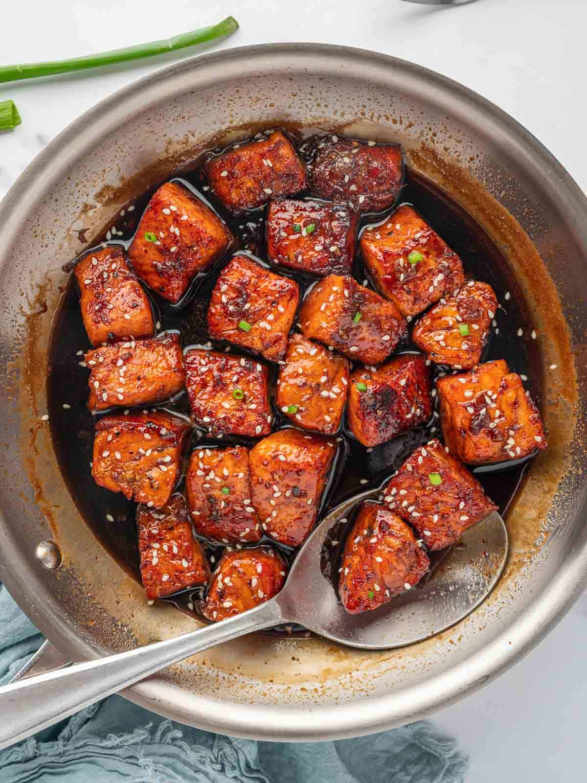 A spoon stirs salmon with honey garlic soy sauce in a skillet.