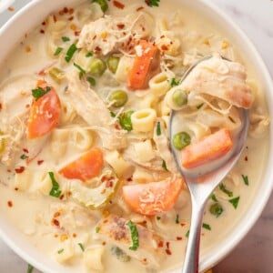 A spoon scoops creamy chicken and vegetable soup from a bowl.