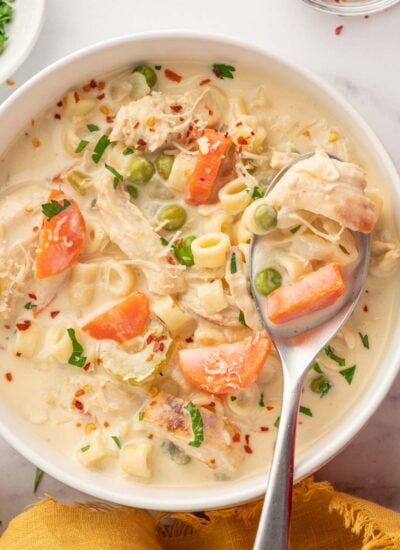 A spoon scoops creamy chicken and vegetable soup from a bowl.