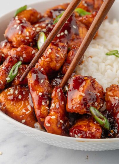 Chopsticks pick up a chicken in gochujang sauce.