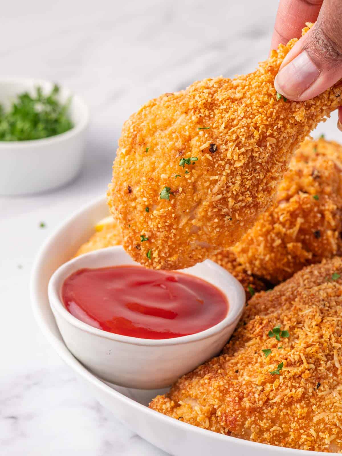 A keto fried chicken leg is dipped in sauce.