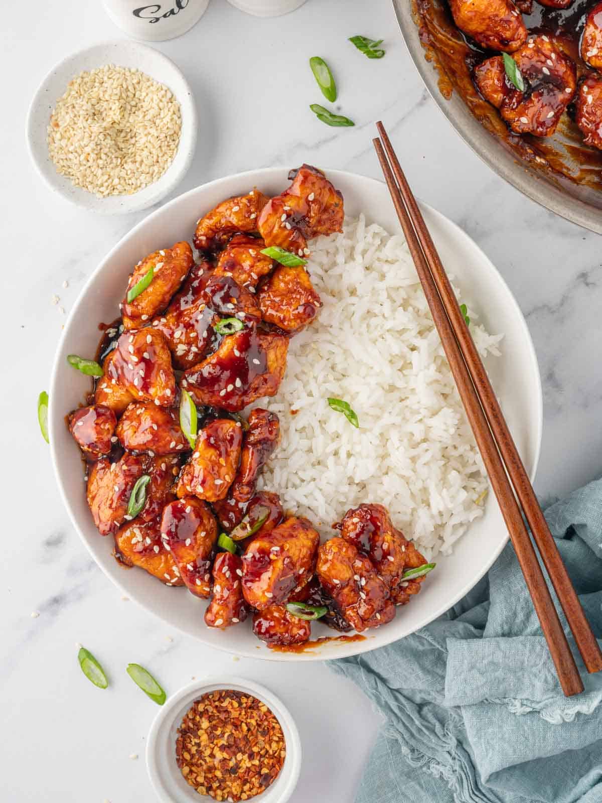 Crispy gochujang chicken bites over a bed of rice with chopsticks.