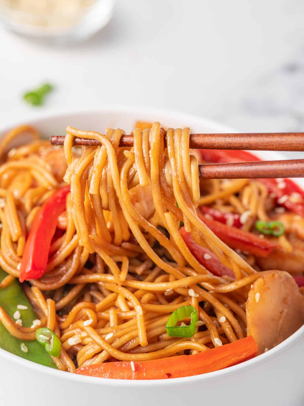 Chopsticks pick up shrimp noodles from a bowl.