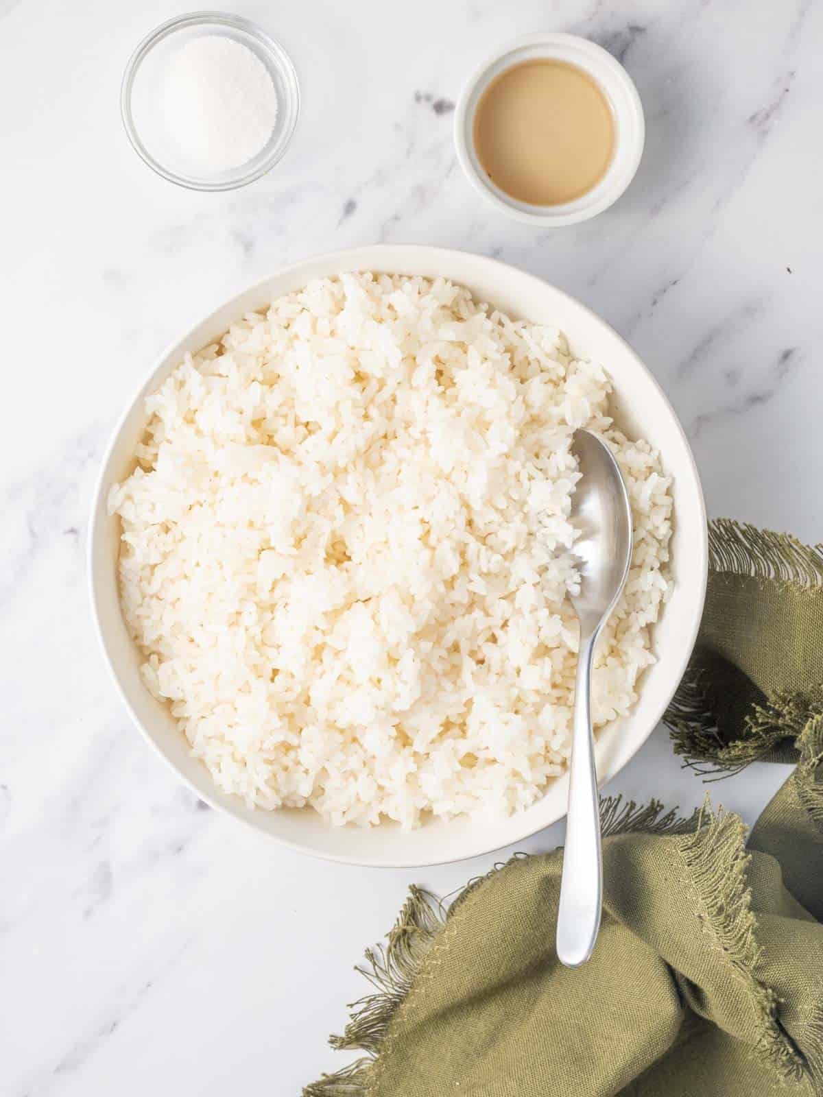 A spoon stirs a bowl of sushi rice with sugar and rice vinegar.