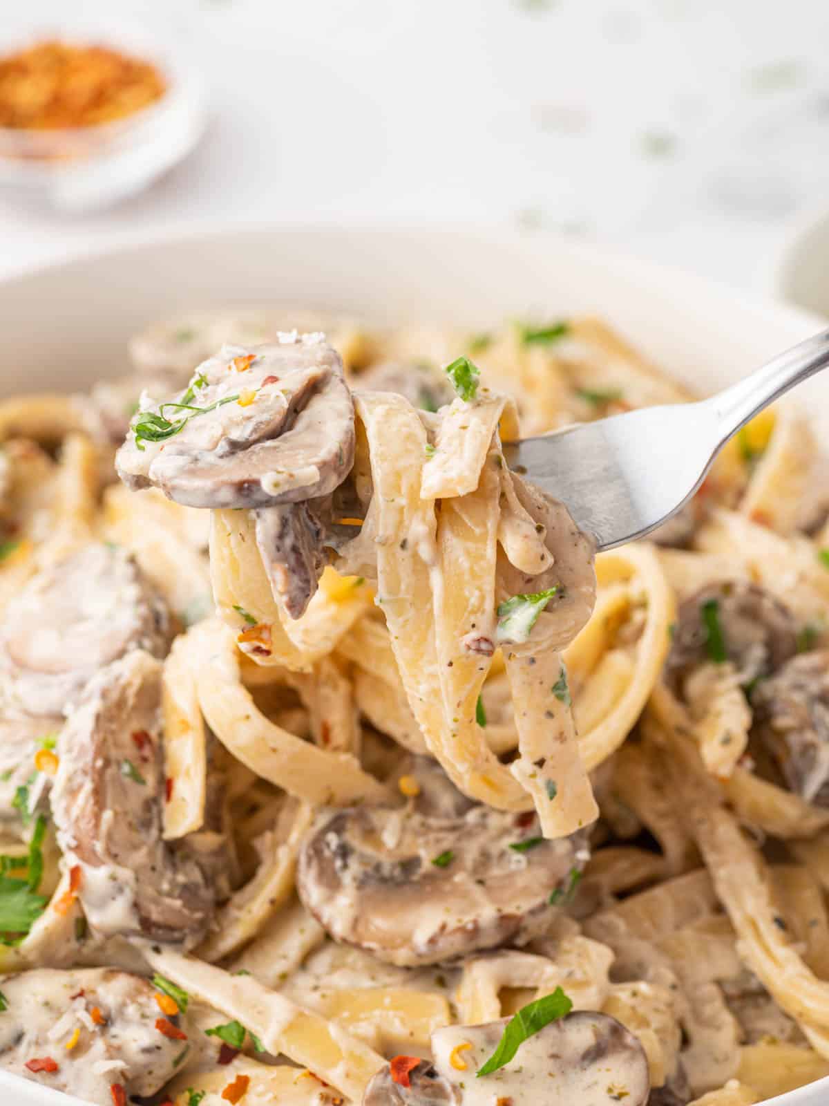 A fork picks up a scoop of fettuccine with mushroom sauce.