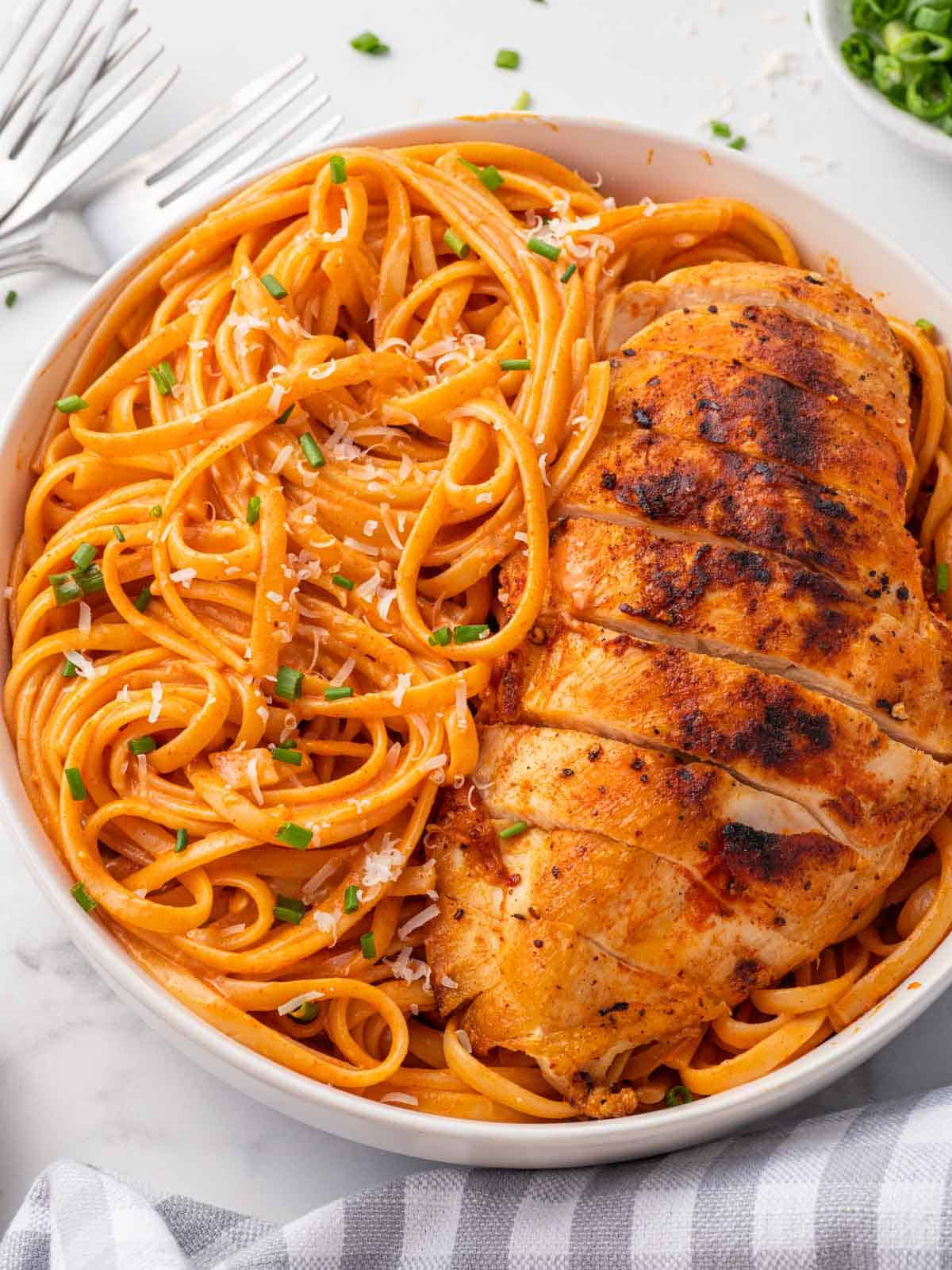 Spicy pasta on a plate with a side of chicken.