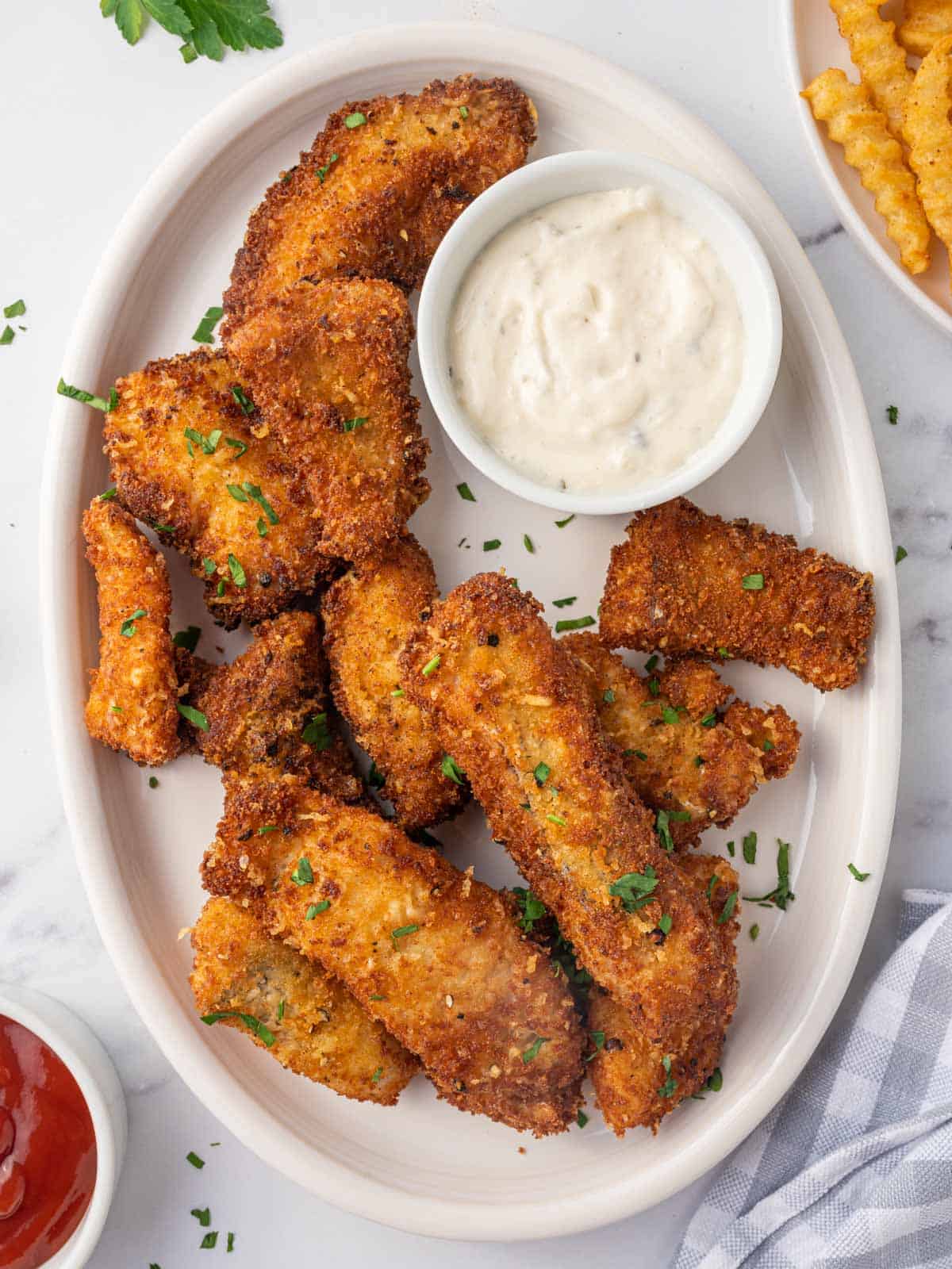 A plate of crispy fish strips with a bowl of tarter sauce.