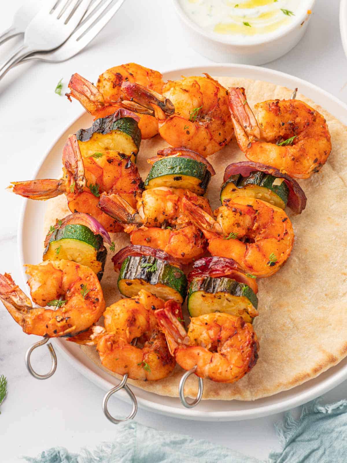 Three shrimp skewers on a pita with dipping sauce.