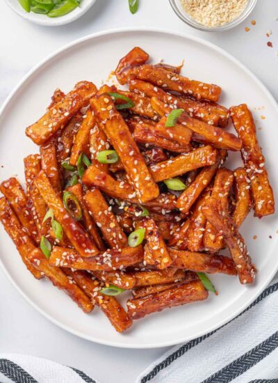 A plate of chilli fries topped with sesame seeds and green onions.