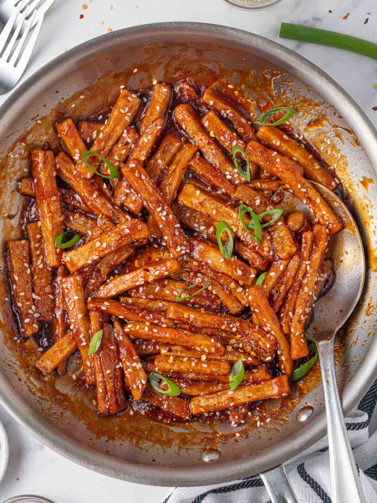 A skillet of sweet chilli potatoes with a spoon.