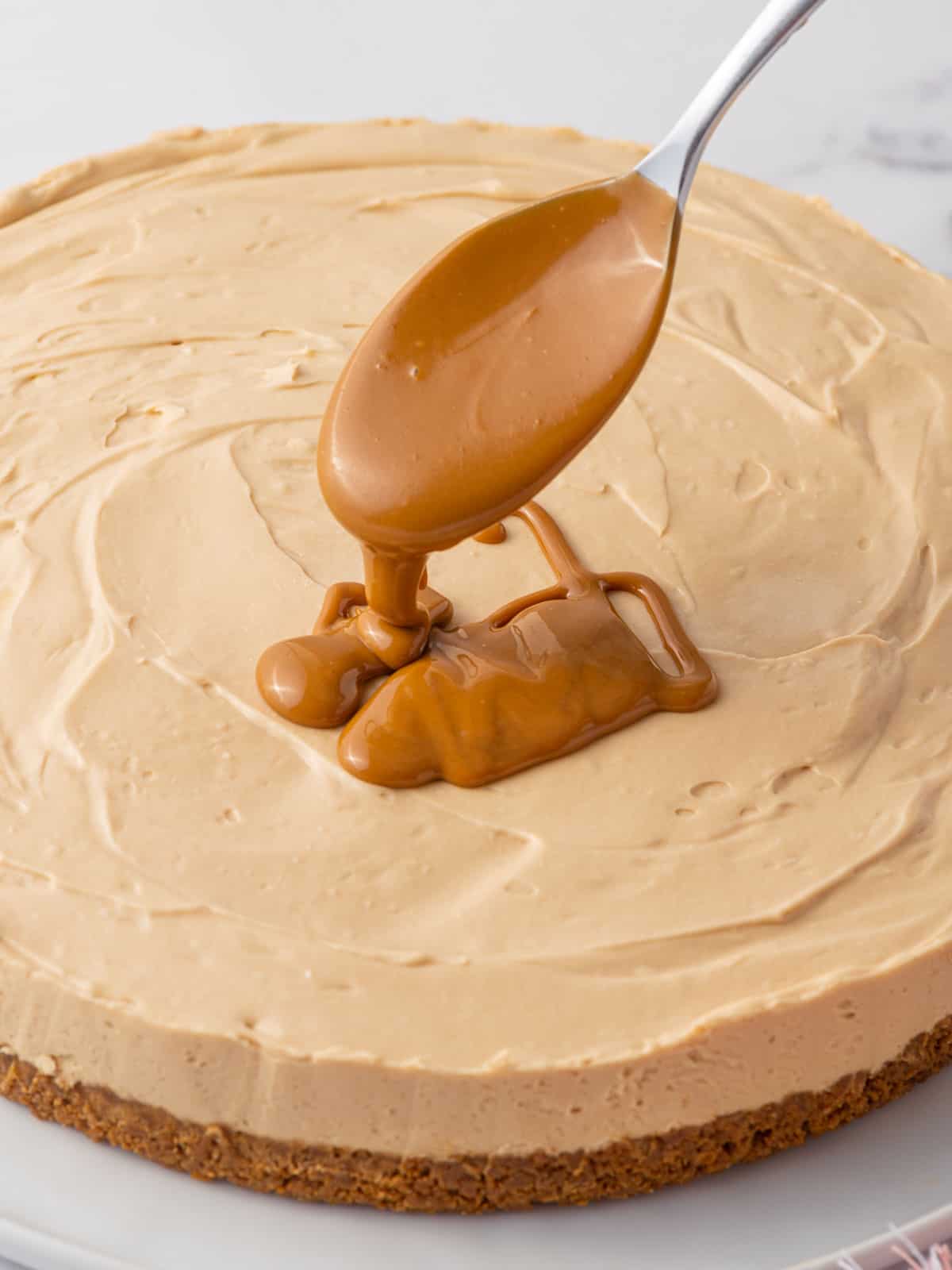 A spoon drizzles melted biscoff spread onto a cheesecake.