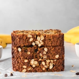 A stack of banana bread slices with bananas in the background.