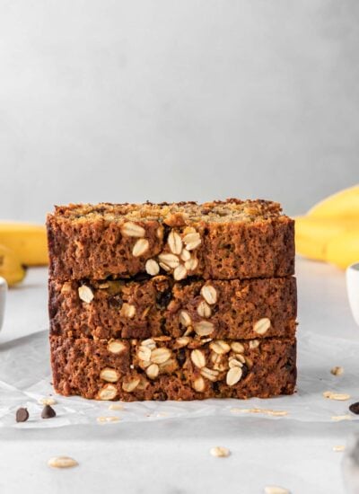 A stack of banana bread slices with bananas in the background.