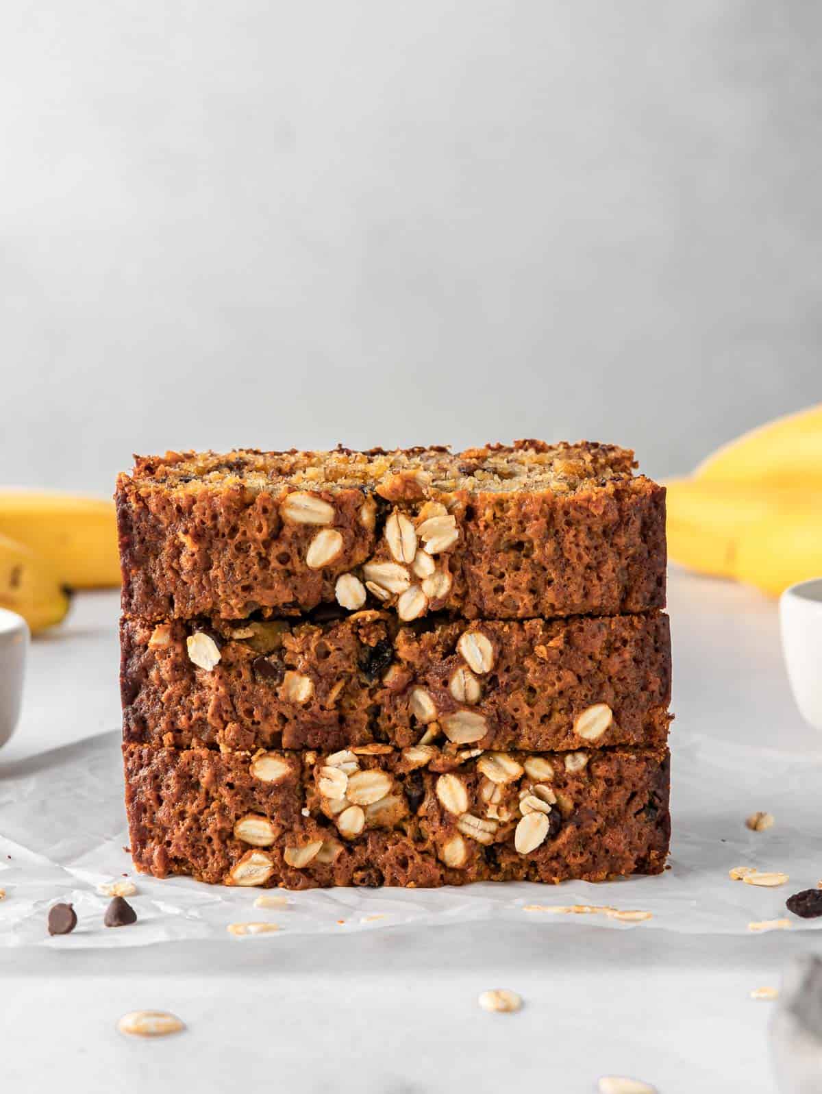 A stack of banana bread slices with bananas in the background.