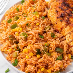 A helping of mexican fried rice on a plate with grilled chicken.