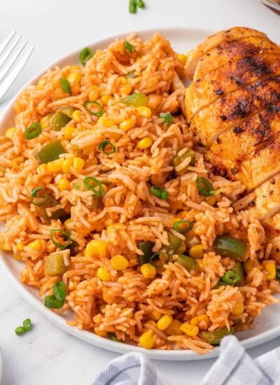 A helping of mexican fried rice on a plate with grilled chicken.