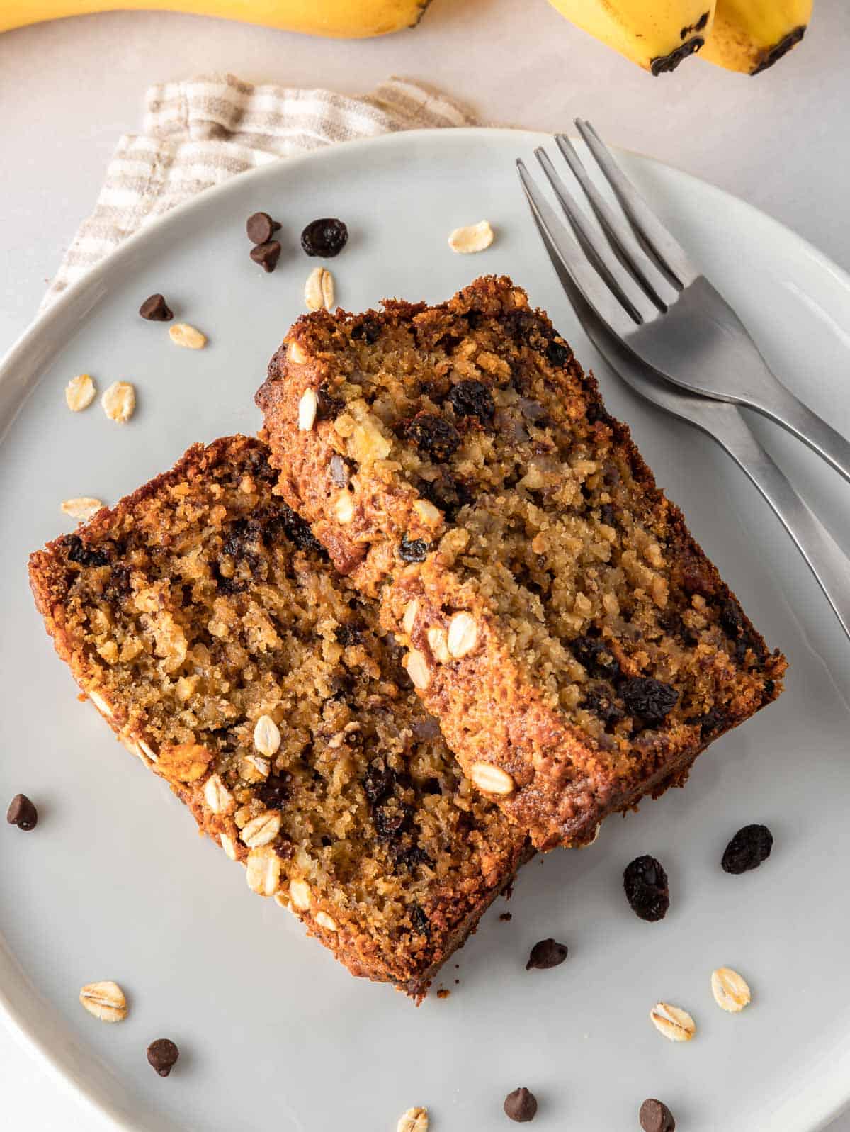 Two slices of banana bread with oats on a plate with two forks.