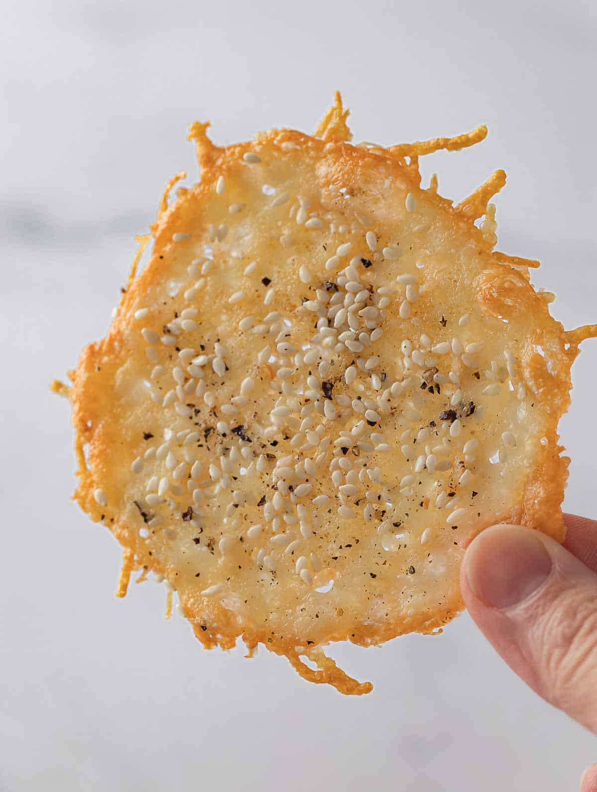 Fingers hold up a crispy parmesan chip.