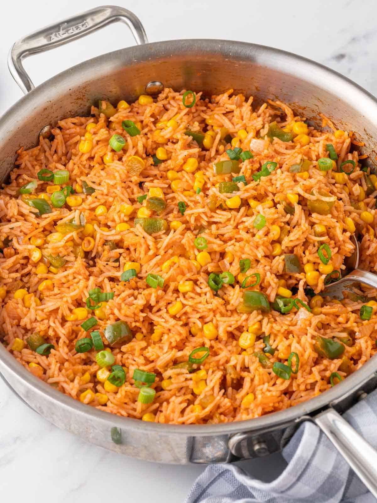 A spoon scoops fried mexican rice from a skillet.