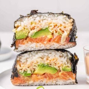 Sliced sushi burger showing layers of salmon, avocado, imitation crab, rice, and nori.