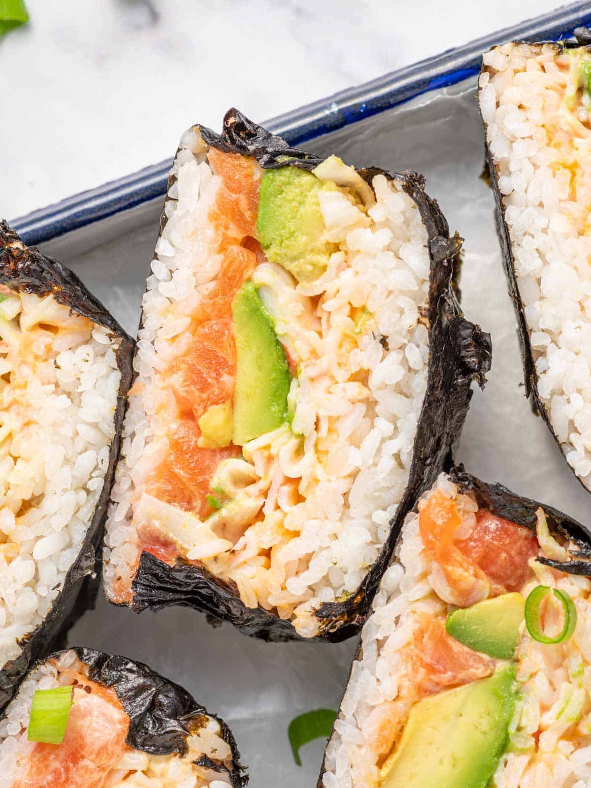 Close-up of a sushi burger with salmon, avocado, imitation crab, rice, and nori.