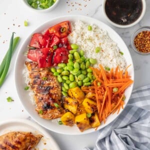 A teriyaki chicken rice bowl with condiments on the side.